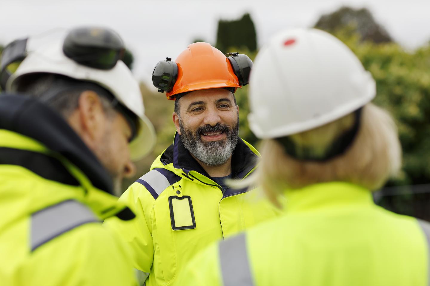 Tre bygg- eller anleggsarbeidere med verneutstyr som snakker sammen