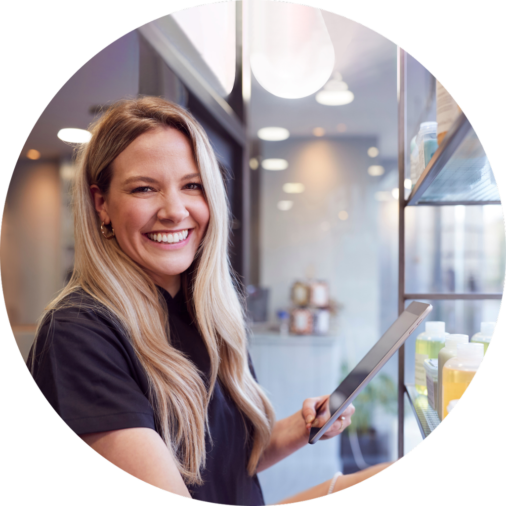 Person i frisørsalong med iPad i hendene foran en hylle med hårprodukter